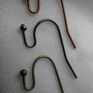 Peut inclure: Trois crochets de boucles d'oreilles de différentes couleurs : cuivre, noir et or. Les crochets sont tous de la même taille et de la même forme, avec une petite boule en haut.