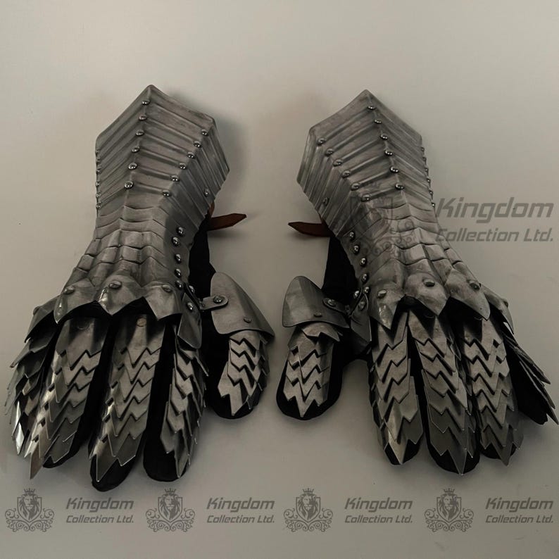 May include: A pair of silver metal gauntlets with a scaly design. The gauntlets are made of interlocking metal plates and have a pointed finger design.