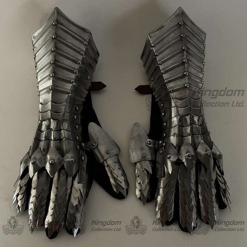 May include: A pair of silver metal gauntlets with a scaly design. The gauntlets are fully articulated and have a pointed design at the top. The gauntlets are made of metal and have a silver finish.