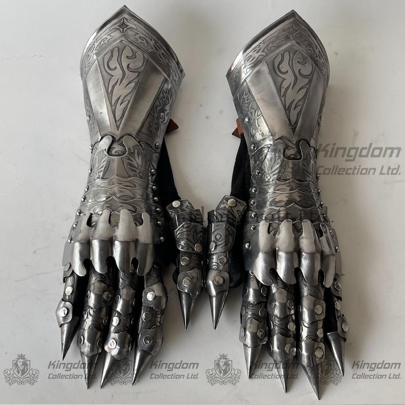 May include: A pair of silver medieval gauntlets with claw-like finger tips and intricate engraved designs. The gauntlets are made of metal and have a leather lining. The gauntlets are displayed on a white background.