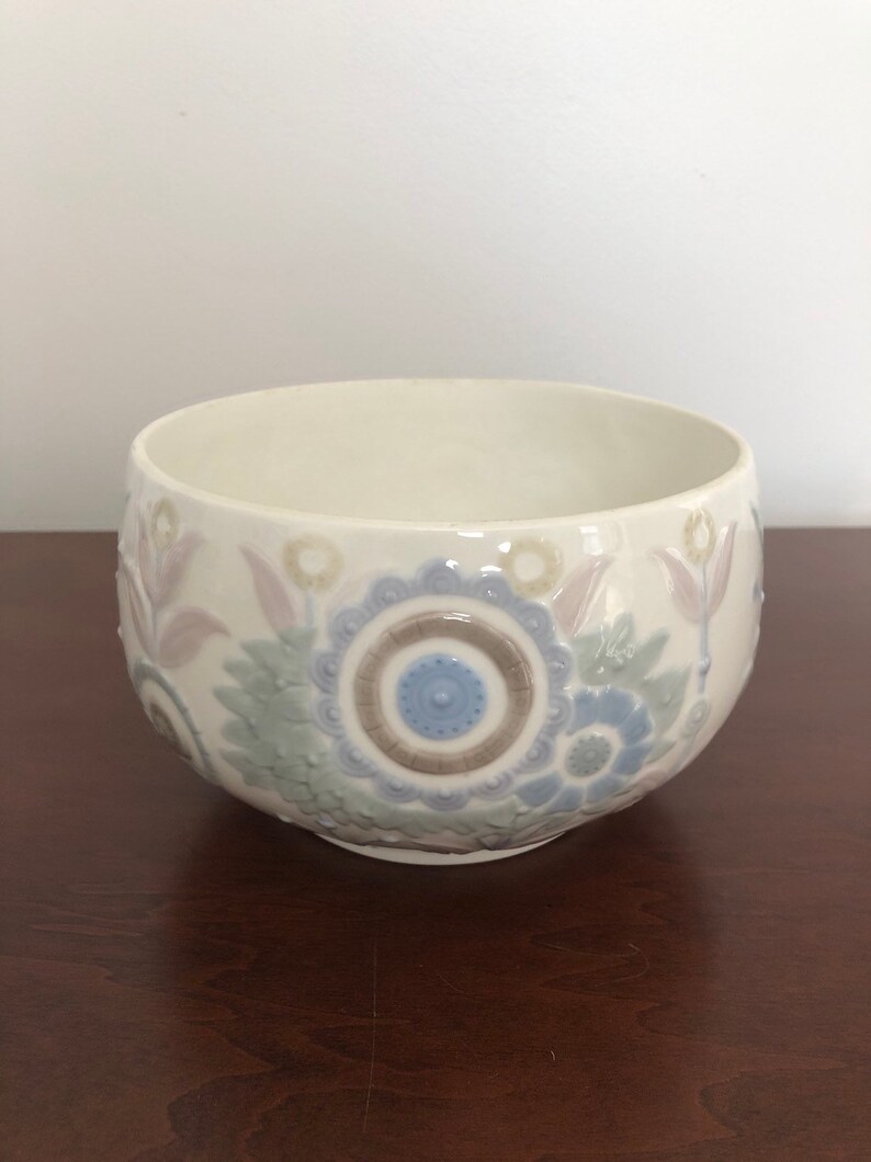 May include: A white ceramic bowl with a floral design in shades of blue, green, and brown. The bowl has a raised design and a glossy finish.