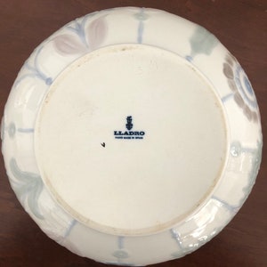 May include: A white ceramic bowl with a blue and gray floral design. The bowl is marked with the Lladro logo and "Hand Made in Spain".
