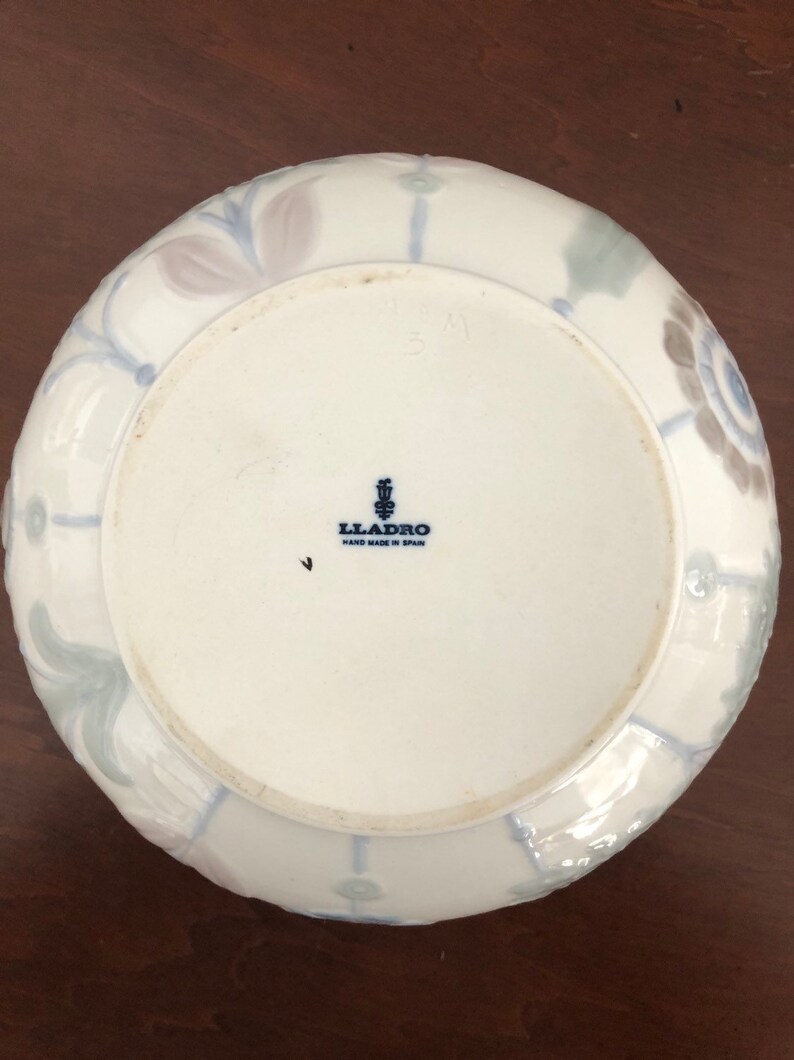 May include: A white ceramic bowl with a blue and gray floral design. The bowl is marked with the Lladro logo and "Hand Made in Spain".