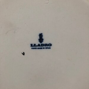 May include: A white porcelain figurine with a blue and white Lladro logo and the text "Hand Made in Spain". The figurine is marked with the number "218M 3".
