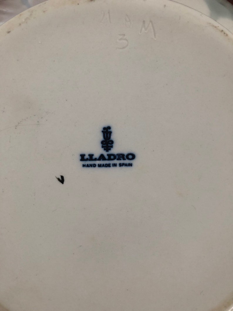 May include: A white porcelain figurine with a blue and white Lladro logo and the text "Hand Made in Spain". The figurine is marked with the number "218M 3".