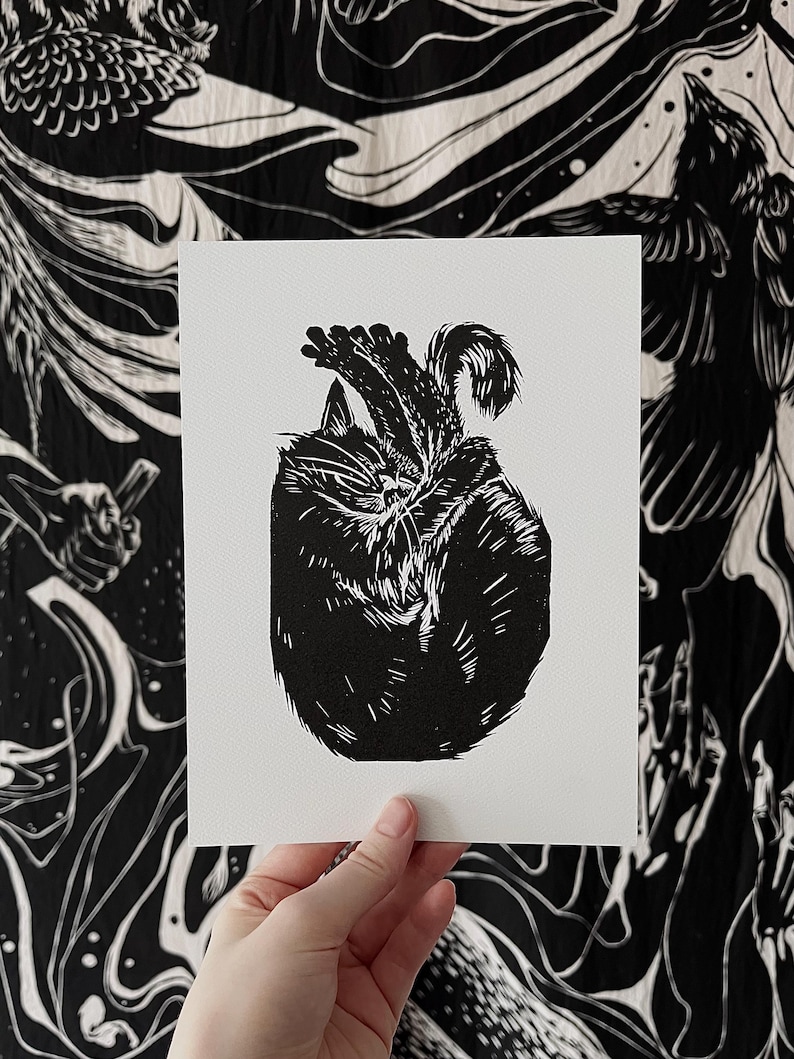 May include: Black and white linocut print of a cat curled up sleeping. The cat is depicted in a simple, minimalist style.