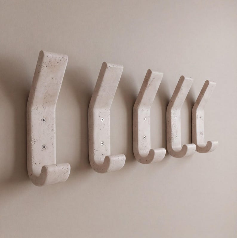 May include: A set of five off-white, curved wall hooks. Each hook is mounted with two screws and has a rounded, downward-facing hook. The hooks are made of a textured material and are mounted on a neutral-colored wall.
