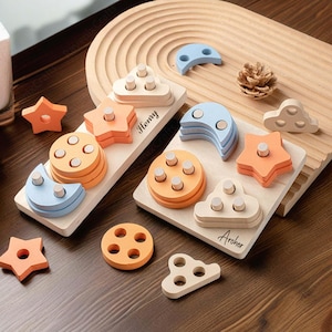May include: Two wooden toy puzzle boards with different shapes and colours. The board on the left has a blue crescent moon, a star, and a circle with pegs. The board on the right has a cloud, a star, a crescent moon, and a circle with pegs. The boards are personalised with the names "Henry" and "Archer".