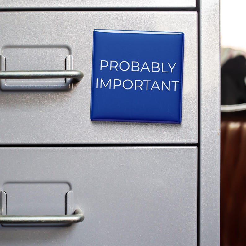 May include: A blue square label with the text "PROBABLY IMPORTANT" in white lettering is affixed to a gray metal file cabinet. The cabinet has two drawers with silver handles.
