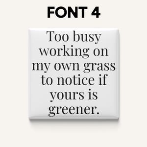 May include: A white square button with the text "Too busy working on my own grass to notice if yours is greener" in black font. The text "FONT 4" is at the top.