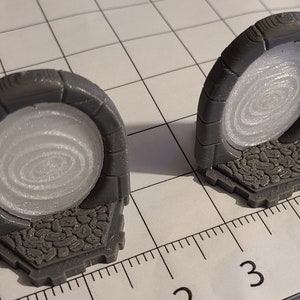 May include: Two grey 3D printed miniature stone archways with a swirling white portal design. The archways are on a white grid background with a ruler in the foreground.