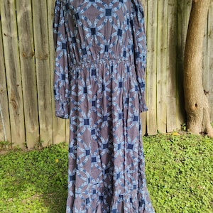 May include: A long-sleeved, blue and gray dress with a geometric pattern. The dress has a high neck and a gathered waist. The fabric has a quilted texture.