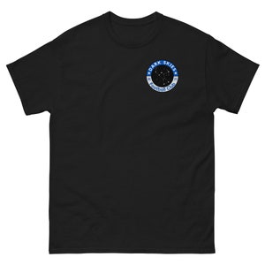Pode incluir: Camiseta preta com um logotipo circular azul e branco que diz "Dark Skies Football Club" com uma constelação dentro do círculo.