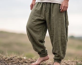 May include: Olive green loose-fitting trousers featuring a gathered elastic waistband with a drawstring tie and elasticated cuffs at the ankles. The trousers have a relaxed, baggy silhouette with a textured fabric finish and a mid-rise fit.