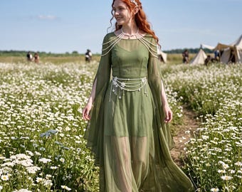 May include: An olive green floor-length dress with long, flowing split sleeves and a sheer overlay. The garment features a white pearl-beaded harness draped over the shoulders and a matching pearl-beaded waist belt with white floral accents.