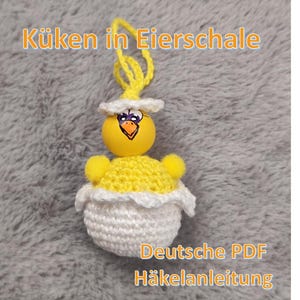 Può includere: Ornamento pasquale fatto a mano con un pulcino giallo all'interno di un guscio d'uovo all'uncinetto bianco e giallo. Il pulcino ha un viso dipinto e un anello giallo per appenderlo. I testi "Küken in Eierschale" e "Deutsche PDF Häkelanleitung" sono visibili.