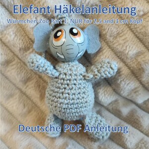 May include: A handmade, light gray crocheted elephant toy with a painted head. The elephant has large eyes, blue ears, and a trunk. The text "Elefant Häkelanleitung" and "Deutsche PDF Anleitung" are visible. The toy is part of the "Würmchen-Zoo Part 1" series.