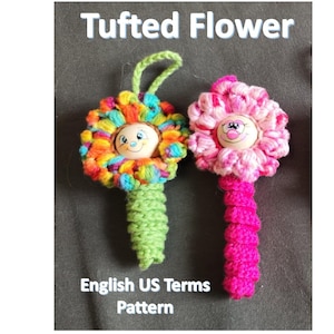 May include: Two handmade, colorful, tufted flower ornaments. One flower is multi-colored with a green stem, and the other is pink with a fuchsia stem. Each flower has a smiling face in the center. The text "Tufted Flower" and "English US Terms Pattern" are visible.