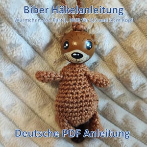 May include: A handcrafted brown crochet otter with a painted wooden head. The otter features a detailed face and is part of a crochet pattern. The image includes the text "Biber Häkelanleitung" and "Deutsche PDF Anleitung".