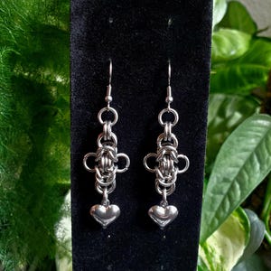 May include: A pair of silver earrings with a heart charm hanging from a chain link design.