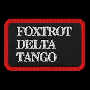 Pode incluir: Um remendo preto com borda vermelha e texto bordado em branco que diz "FOXTROT DELTA TANGO".