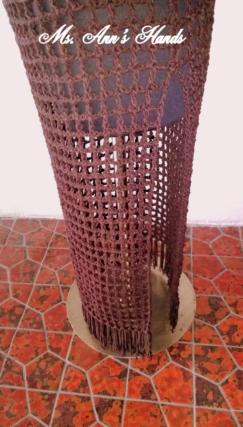 May include: A brown crocheted skirt with fringe on the bottom. The skirt is displayed on a mannequin and the text "Ms. Ann's Hands" is visible at the top of the skirt.