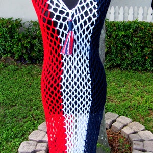 Peut inclure: Une robe en crochet rouge, blanche et bleue avec un pompon. La robe est faite d'un tissu en maille et a un col en V.