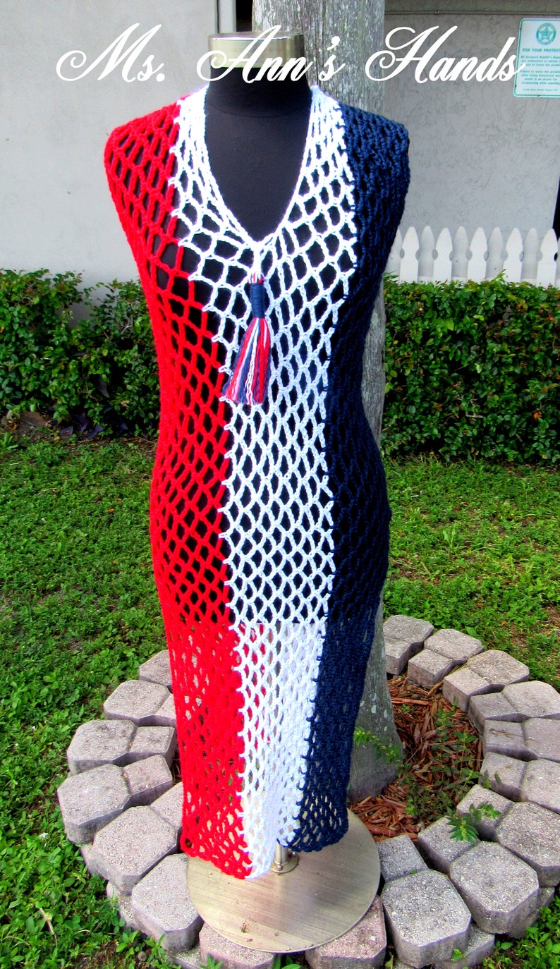 Peut inclure: Une robe en crochet rouge, blanche et bleue avec un pompon. La robe est faite d'un tissu en maille et a un col en V.