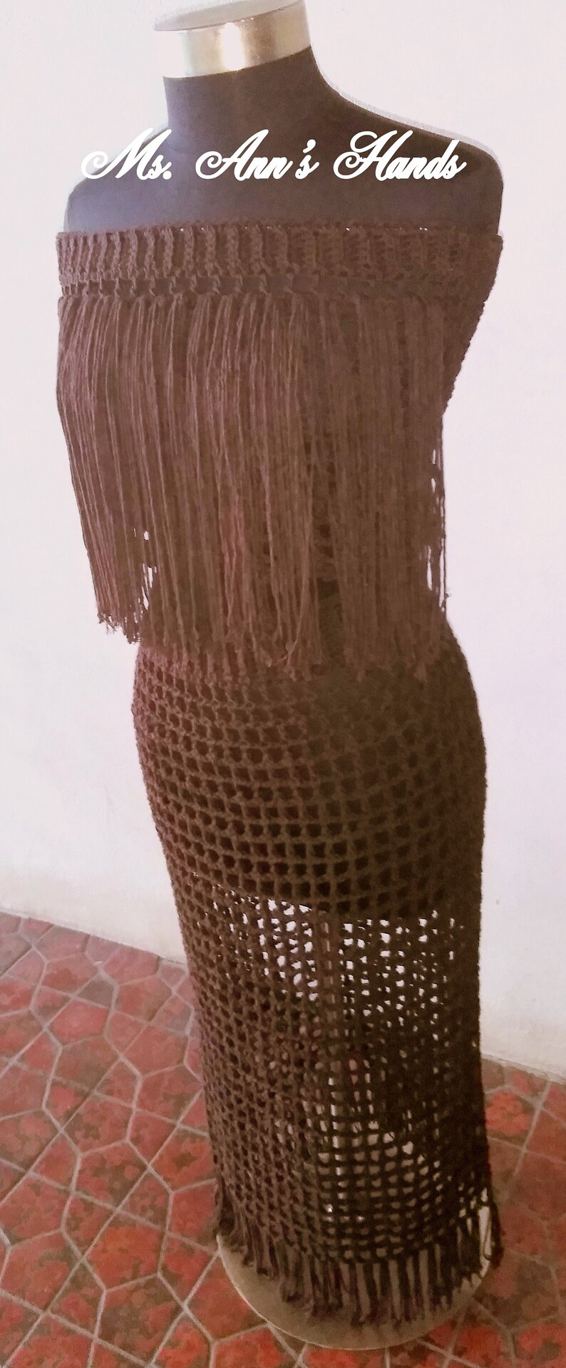 May include: A brown crochet dress with fringe detailing. The dress is on a mannequin and has a square neckline.
