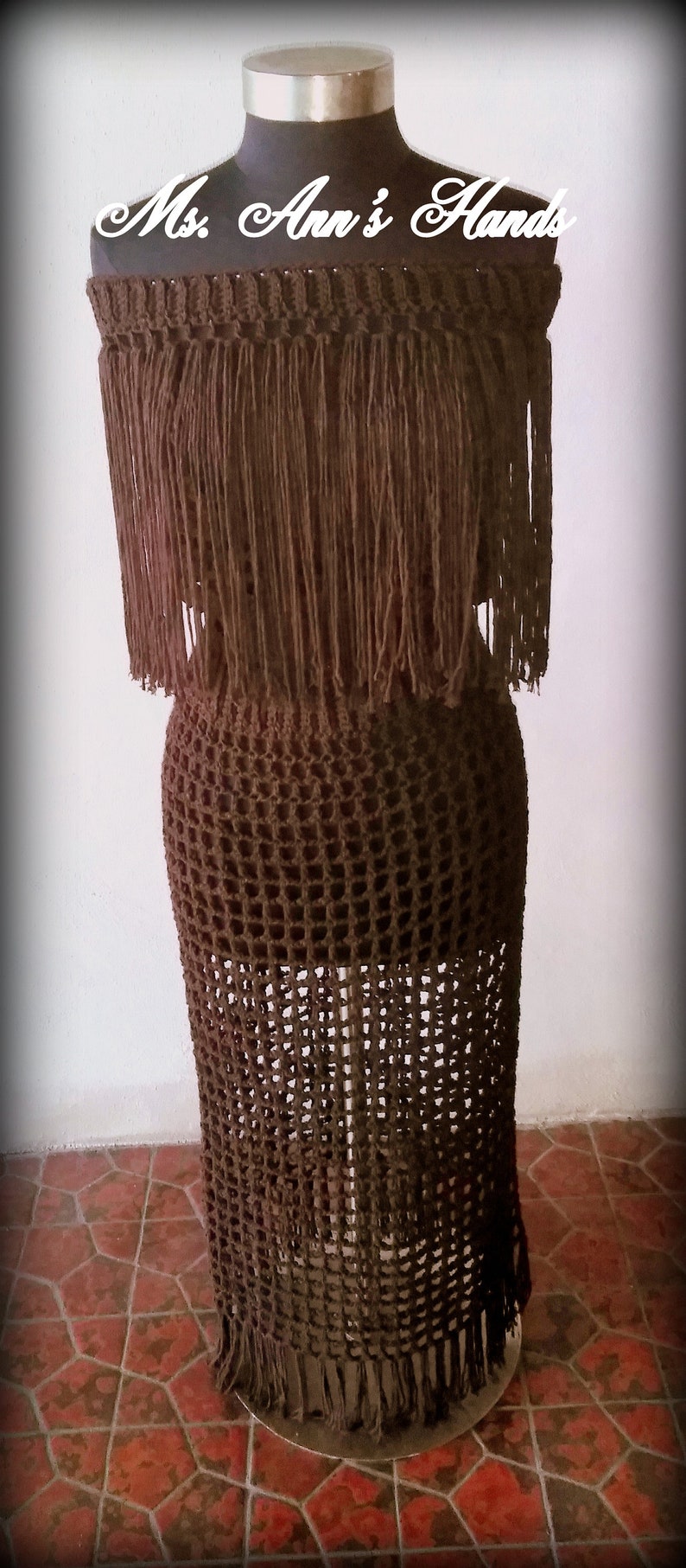 May include: A brown crochet dress with fringe detailing. The dress is on a mannequin and the text "Ms. Ann's Hands" is visible at the top of the image.