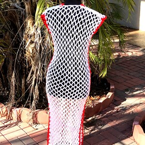 Peut inclure: Robe maxi en crochet blanc avec des bordures rouges. La robe est sans manches et a une coupe ample. Elle est pr&eacute;sent&eacute;e sur un mannequin.