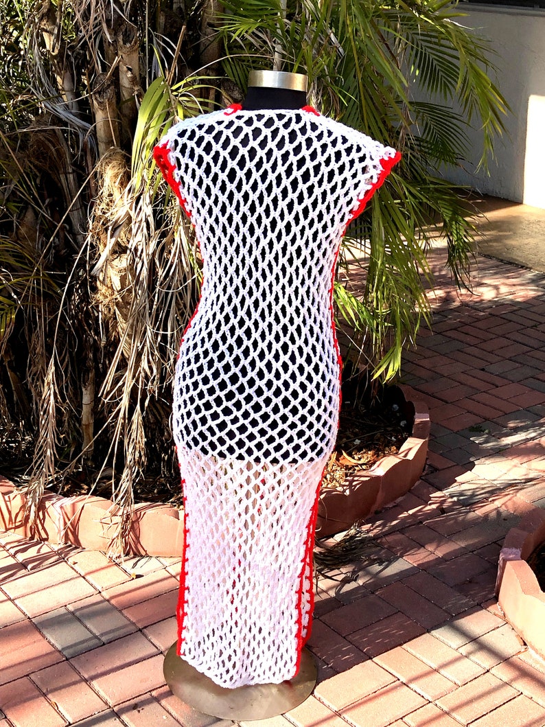 Peut inclure: Robe maxi en crochet blanc avec des bordures rouges. La robe est sans manches et a une coupe ample. Elle est pr&eacute;sent&eacute;e sur un mannequin.