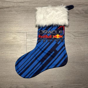 Può includere: Calza di Natale blu e navy con il logo Oracle Red Bull Racing. La calza ha un polsino in finta pelliccia bianca e un anello per appenderla. Il corpo della calza presenta strisce diagonali.