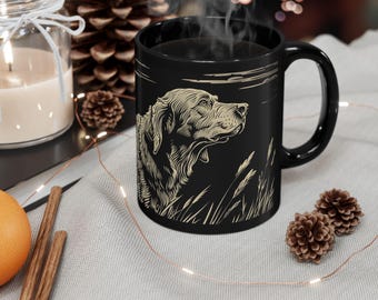 Könnte beinhalten: Schwarze Keramik-Kaffeetasse mit einer weißen Silhouette eines Hundekopfes, der nach rechts schaut. Der Hund befindet sich in einem Feld mit hohem Gras.