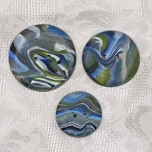May include: Three round buttons with a swirling blue, green, and white pattern. The buttons have two holes each.