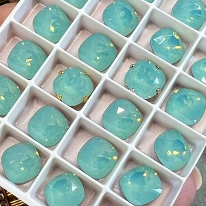 May include: A white plastic tray with 20 square compartments filled with light blue, iridescent, square-shaped rhinestones.