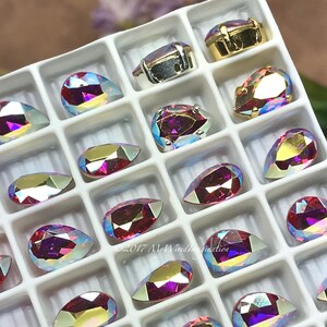 Puede incluir: Una bandeja con pedrer&iacute;a iridiscente en varias formas, incluyendo l&aacute;grimas y &oacute;valos. La pedrer&iacute;a tiene un efecto brillante multicolor, con tonos de rosa, morado y dorado. Algunas est&aacute;n engastadas en engastes de metal plateado u dorado. El texto "&copy;2017 MyWiredImagination" es visible.