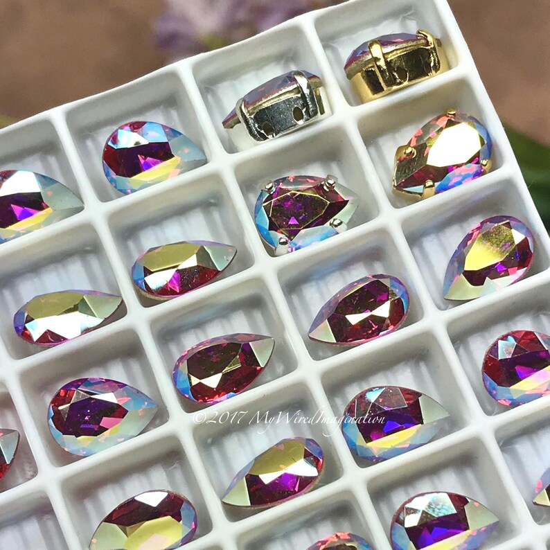Puede incluir: Una bandeja con pedrer&iacute;a iridiscente en varias formas, incluyendo l&aacute;grimas y &oacute;valos. La pedrer&iacute;a tiene un efecto brillante multicolor, con tonos de rosa, morado y dorado. Algunas est&aacute;n engastadas en engastes de metal plateado u dorado. El texto "&copy;2017 MyWiredImagination" es visible.