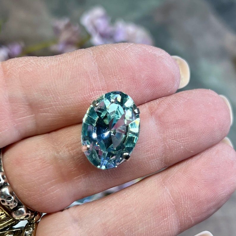 May include: A large, oval-shaped, light blue crystal with a silver setting. The crystal is faceted and has a high shine.