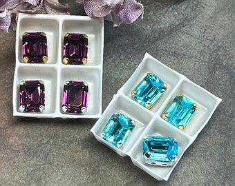 May include: Two sets of four emerald-cut rhinestones in a white plastic storage container. One set is purple and the other is turquoise.