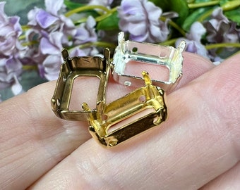 May include: Three metal settings for bezel setting, in gold, silver, and bronze. The settings are rectangular with rounded corners and have four prongs.