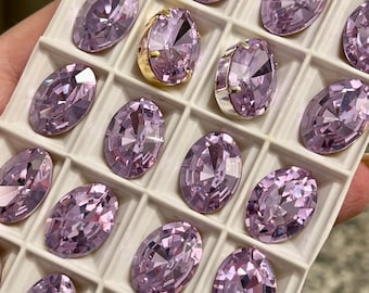 May include: A close-up of a tray of oval-shaped, light purple rhinestones. The rhinestones are arranged in a grid pattern and are all the same size.