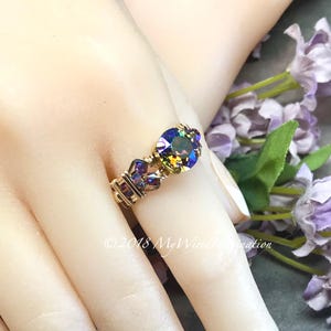 May include: A handcrafted ring with a large, iridescent gemstone and smaller purple accent stones. The ring is made with gold-colored wire, featuring a unique, artistic design. The text "©2018 MyWiredImagination" is visible.