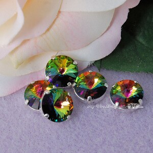 May include: Five iridescent round crystals with silver settings. The crystals display a vibrant spectrum of colors, including green, yellow, orange, and purple. The crystals are arranged on a light purple surface, with a soft pink and white flower in the background.