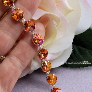 K&ouml;nnte beinhalten: Ein Armband mit einer Reihe runder, facettierter orangefarbener und gelber Kristalle, die in silberfarbenen Metallfassungen sitzen. Die Kristalle haben ein lebendiges, reflektierendes Finish in warmen Farbt&ouml;nen. Der Text My WiredImagination ist sichtbar.