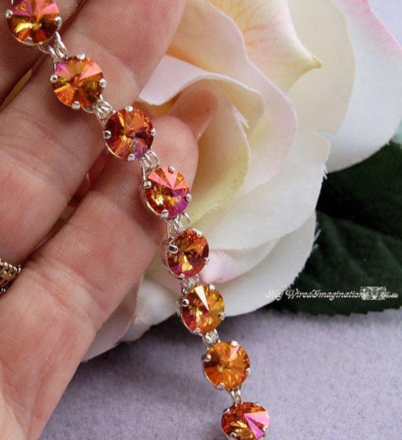 K&ouml;nnte beinhalten: Ein Armband mit einer Reihe runder, facettierter orangefarbener und gelber Kristalle, die in silberfarbenen Metallfassungen sitzen. Die Kristalle haben ein lebendiges, reflektierendes Finish in warmen Farbt&ouml;nen. Der Text My WiredImagination ist sichtbar.