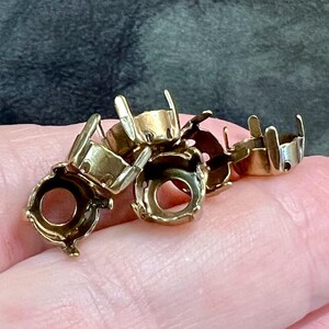 K&ouml;nnte beinhalten: Eine Ansammlung kleiner, goldfarbener Metallfassungen mit kreisf&ouml;rmigen Basen und mehreren aufrechten Krappen, die zur Aufnahme von Edelsteinen dienen. Diese Komponenten sind in einer Gruppe angeordnet und zeigen ihre polierte Oberfl&auml;che.