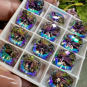 May include: Twelve iridescent gemstone cabochons in a white plastic tray. The gemstones are a mix of purple, blue, green, and gold.