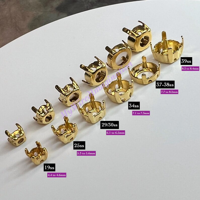 K&ouml;nnte beinhalten: Eine Sammlung goldfarbener Metallfassungen mit Krallen, sortiert nach Gr&ouml;&szlig;e. Beschriftungen zeigen Gr&ouml;&szlig;en von 19ss (4,4 bis 4,6 mm) bis 39ss (8,2 bis 8,4 mm). Diese Komponenten dienen zur Befestigung von Steinen oder Kristallen bei der Schmuckherstellung.