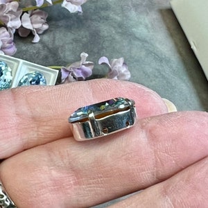 May include: A clear, faceted, iridescent gemstone set in a silver bezel setting. The gemstone is oval shaped and has a rainbow of colors.